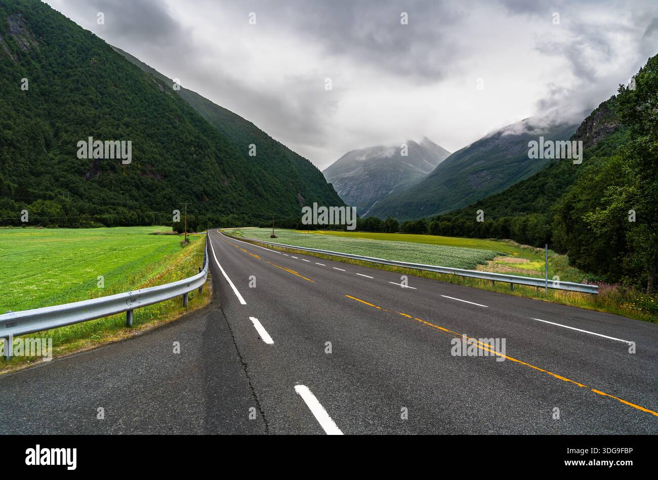 La strada nazionale norvegese 70 si estende attraverso la valle della Sunndalen a Møre og Romsdal. Nuvole scure coprono il cielo sopra le montagne e i campi verdi Foto Stock