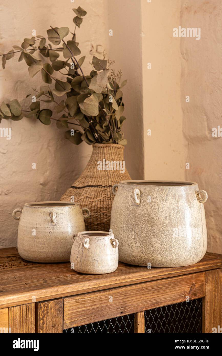 Un ambiente di arredamento tranquillo caratterizzato da tre vasi in ceramica color crema fatti a mano con manici laterali, disposti su un tavolo in legno. Foto Stock