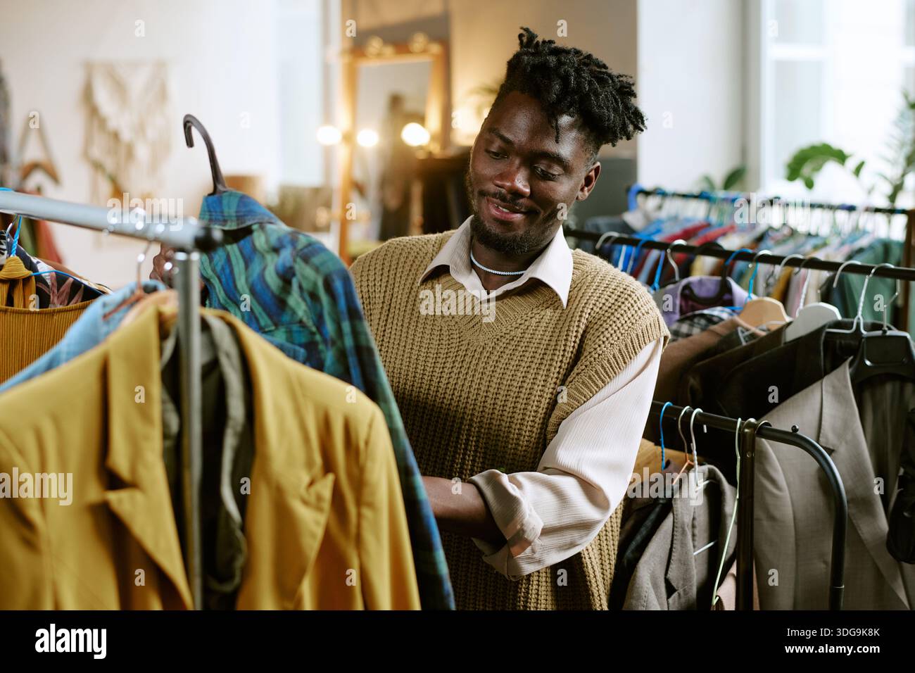 Giovane adulto, uomo Nero, che sfoglia abbigliamento di seconda mano nel Thrift Store Foto Stock
