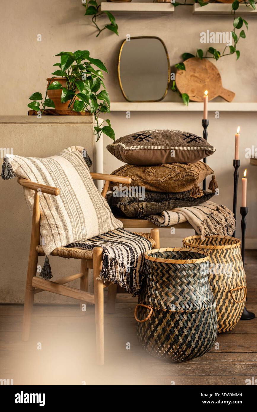 Un ambiente completo di stile interno caratterizzato da una sedia Wishbone di legno chiaro con un cuscino a righe, una pila di cuscini boho su una panca di legno. Foto Stock