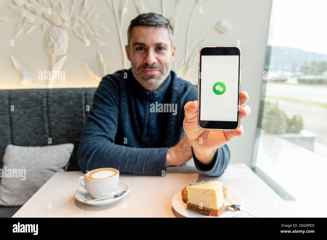 Bar, Montenegro, 9 gennaio 2026, l'uomo chiama o scrive un messaggio tramite la moderna messaggistica mobile WeChat mentre è seduto in un bar Foto Stock