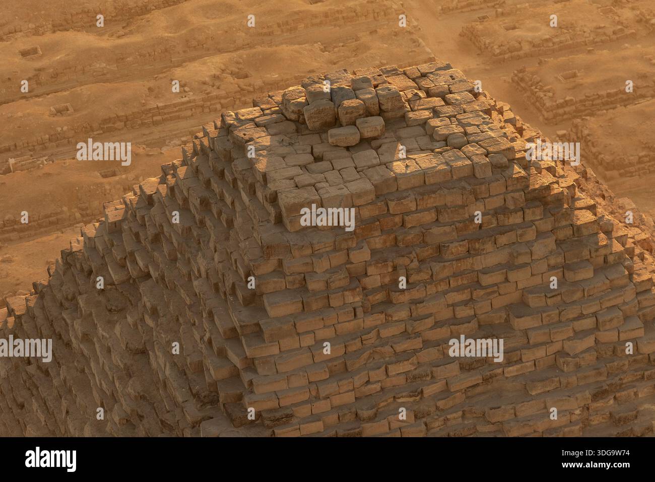 Veduta aerea della cima intemprata di un'antica piramide, i suoi blocchi di pietra bagnati dal caldo bagliore del sole del deserto, Giza, Egitto. Foto Stock