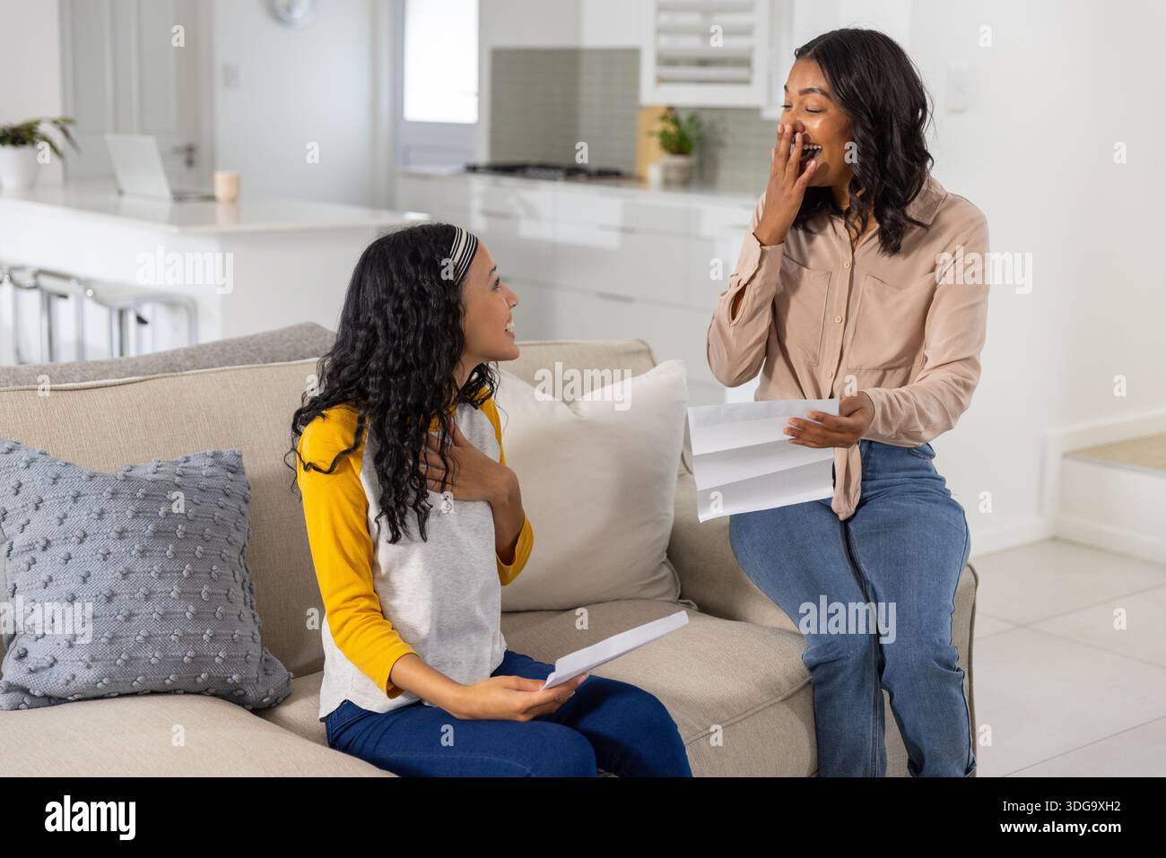 Mamma e figlia adolescente diverse leggono lettere mentre si siedono sul divano beige Foto Stock