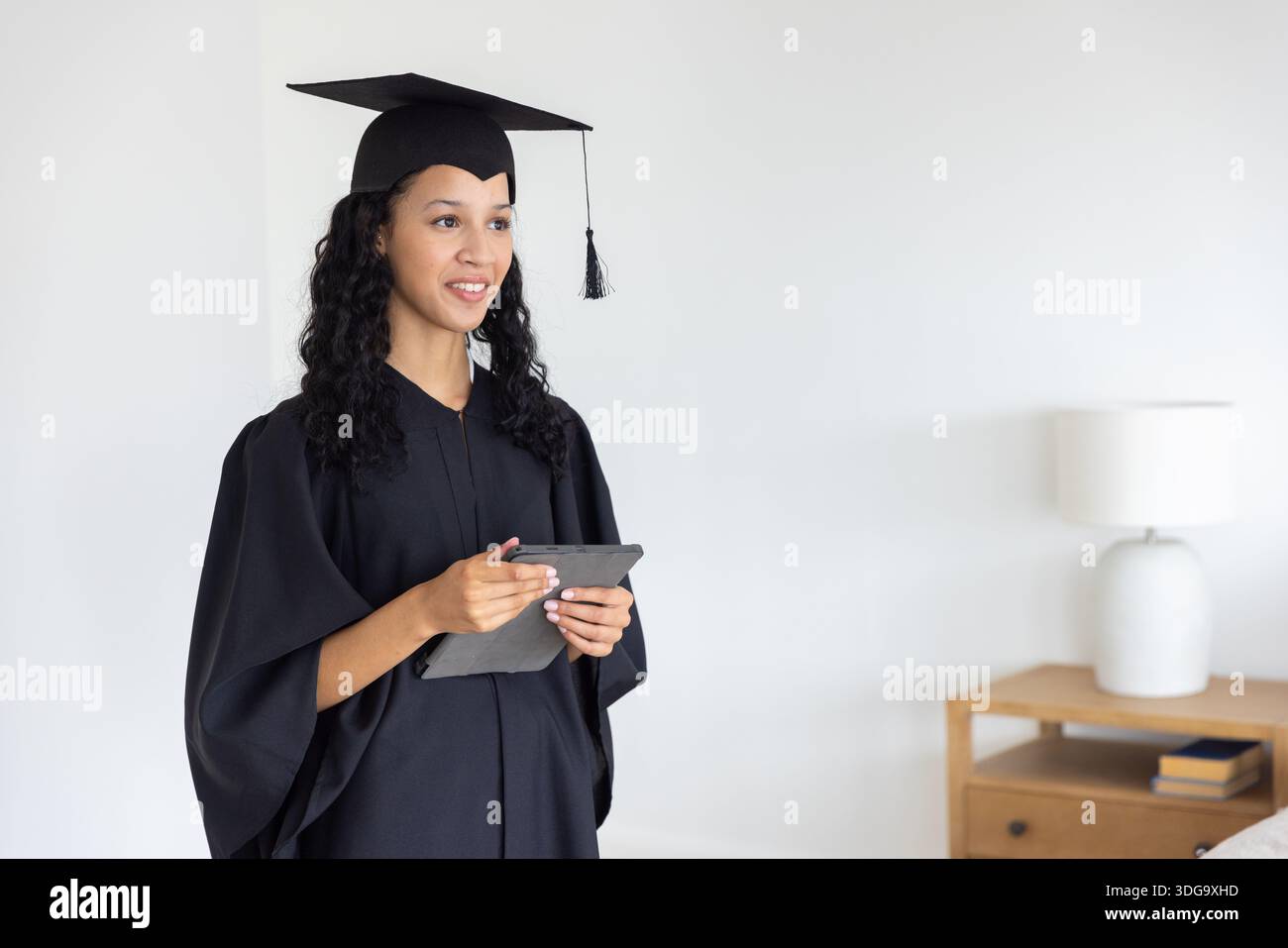 Adolescente in piedi a casa con cappello, abito e tablet con lampada, libri Foto Stock