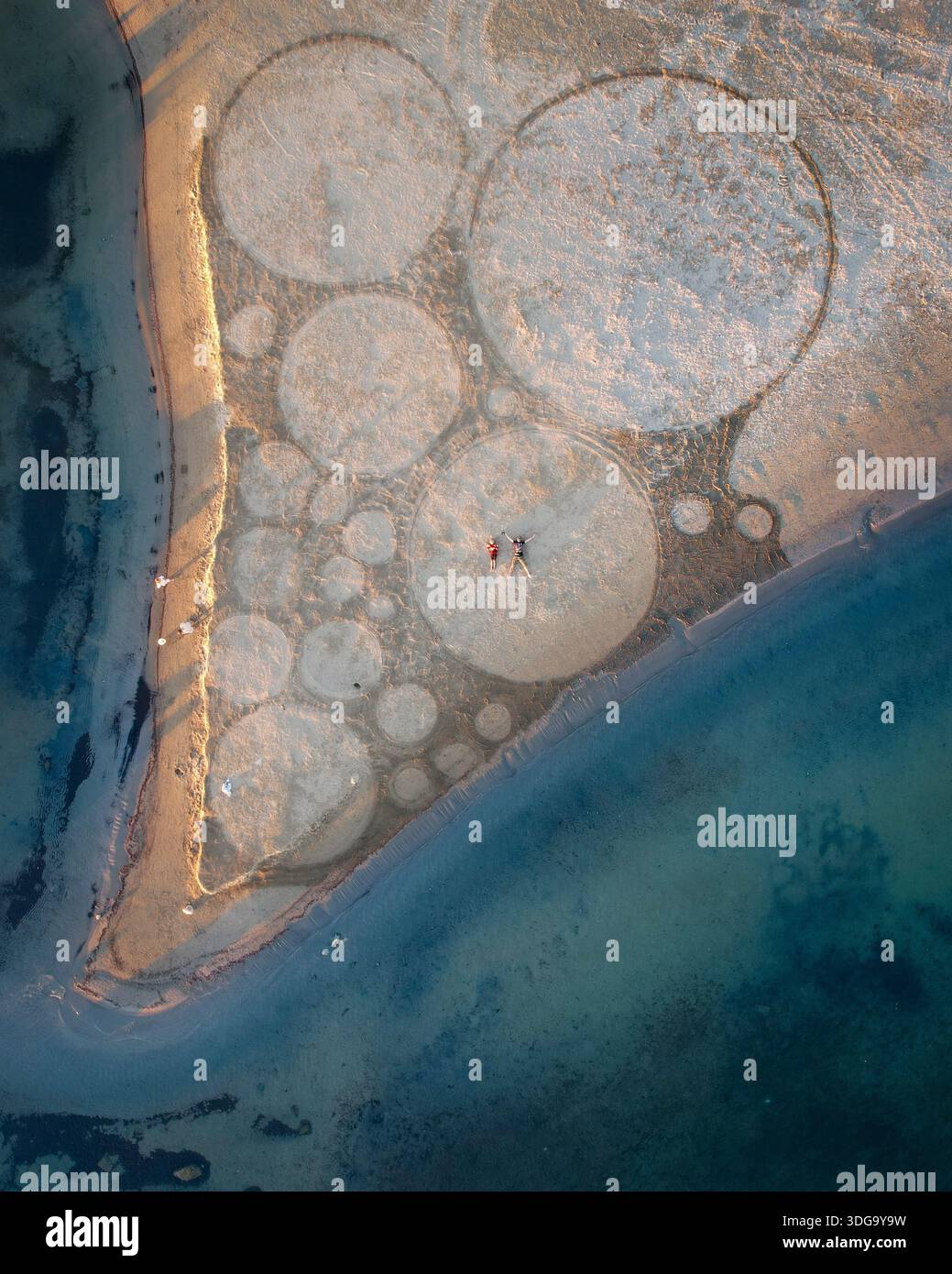 Vista aerea di cerchi geometrici incisi nella sabbia sulla spiaggia di Follonica, una coppia in piedi al centro, dove il mare turchese incontra la riva, Foll Foto Stock