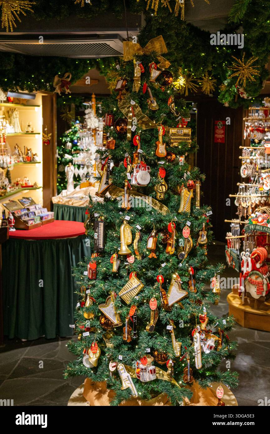Un alto albero di Natale riccamente decorato con ornamenti per strumenti musicali esposti all'interno di un negozio di articoli da regalo. Foto Stock