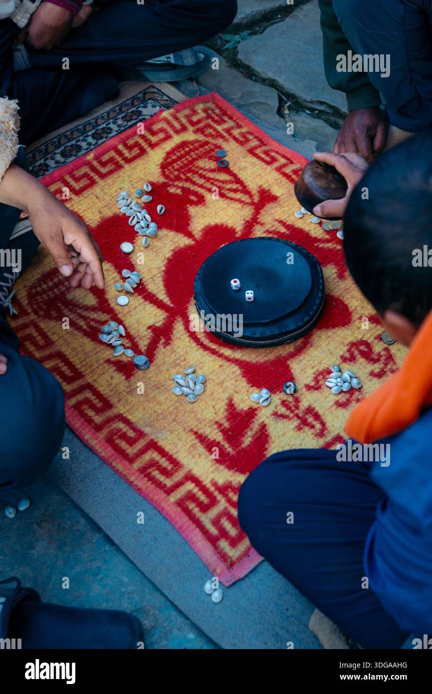 Vista delle persone che giocano a un gioco con monete e ciotole su un tappeto a motivi geometrici, un momento di attività condivisa e scambio culturale, Himalaya, Nepal. Foto Stock