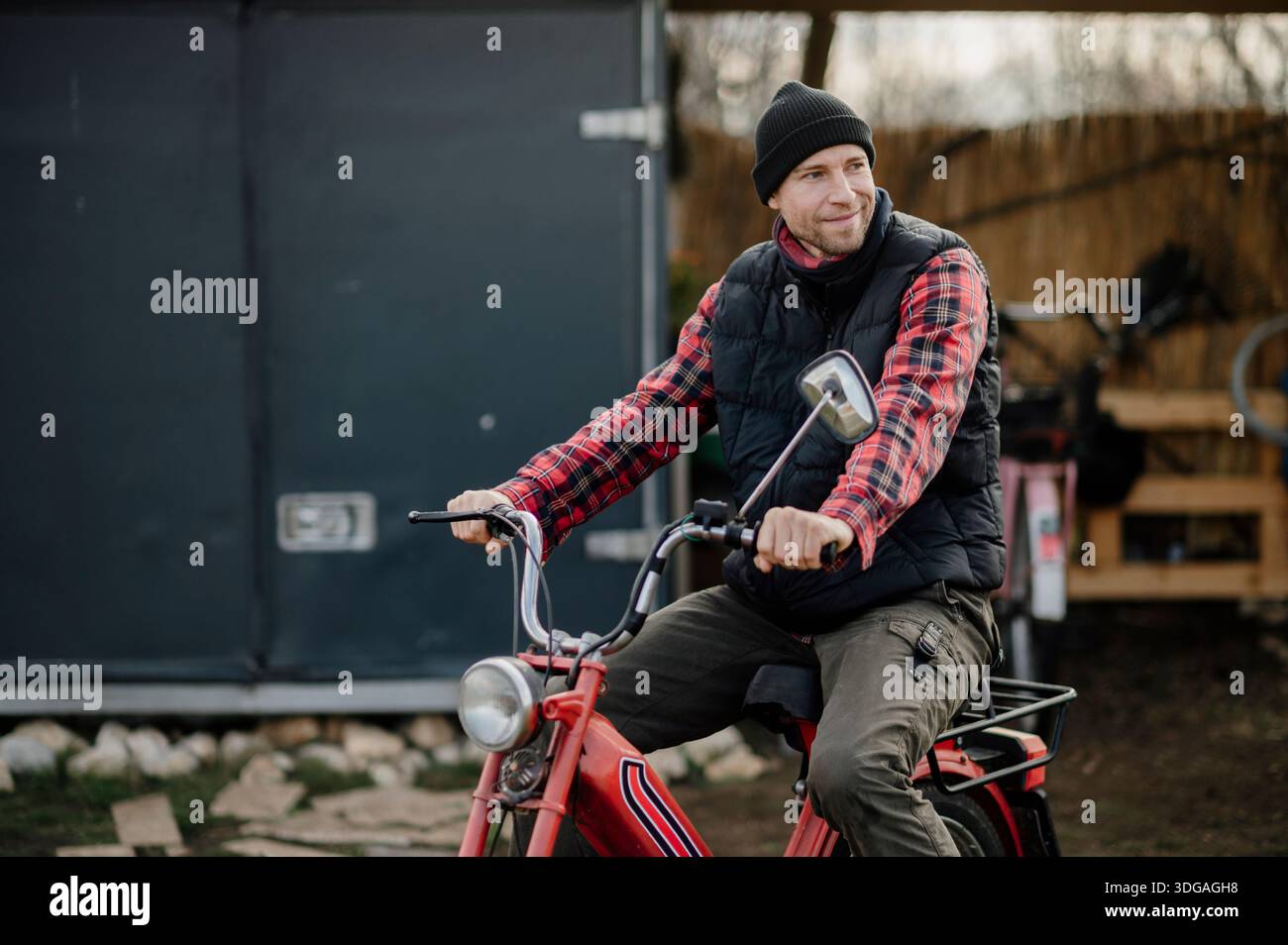 L'uomo guida una bicicletta rossa con un gilet nero e una camicia a quadri Foto Stock