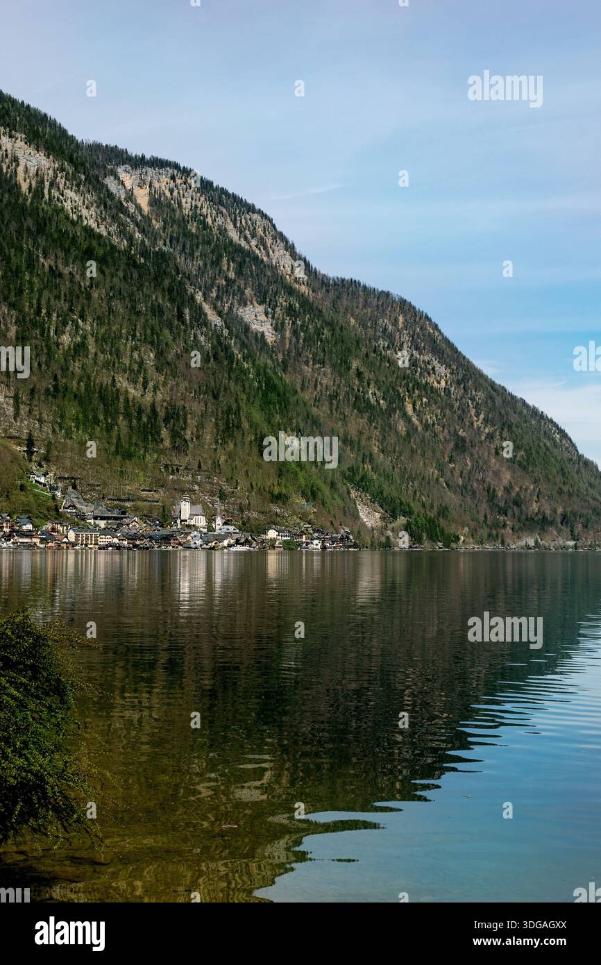 Hallstatt, Austria. Pittoresco villaggio alpino incastonato tra montagna e lago. I piccoli edifici cittadini si riflettono in una superficie di acqua calma con la bocca boscosa Foto Stock