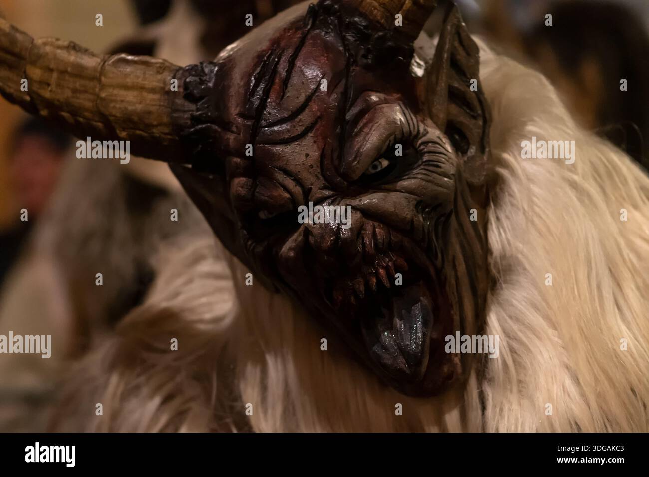 Vista del profilo di Krampus con enormi corna e pelliccia leggera contro la folla serale Foto Stock