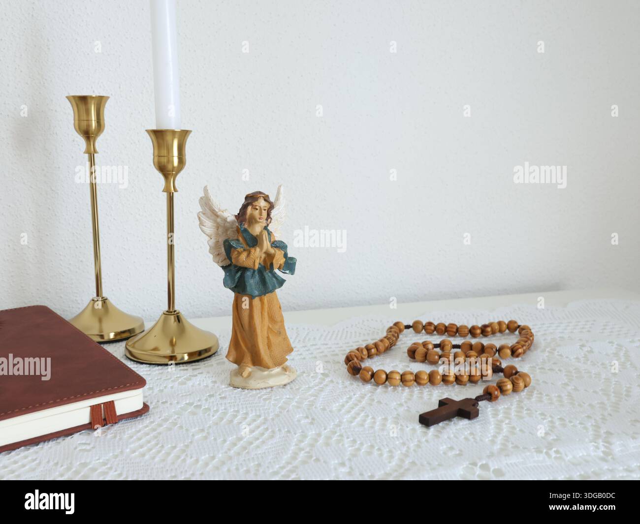 Angolo cattolico a casa. Figurina d'angelo, perline di rosario in legno, croce e libro di preghiere. Fede, simboli e tradizioni. Foto Stock