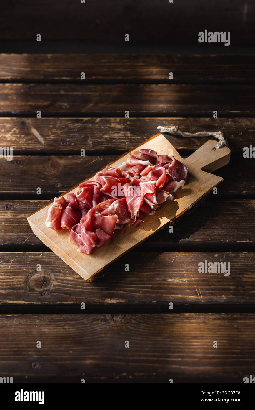 Affettare il prosciutto crudo su un tagliere rustico. Eccellenza gastronomica con luce naturale. Foto Stock