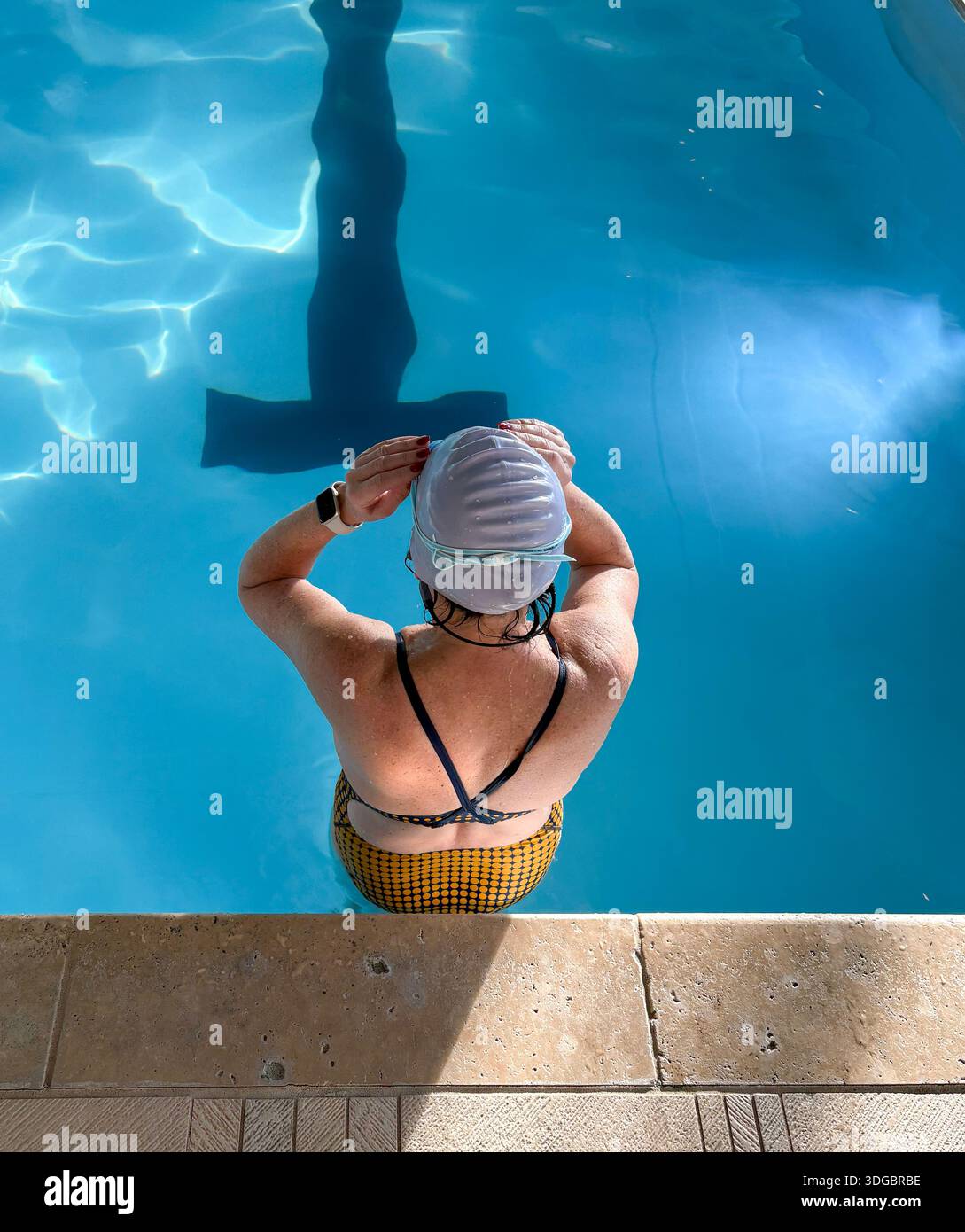 Vista posteriore di una persona che regola il berretto mentre si trova in piscina in piena luce. Foto Stock