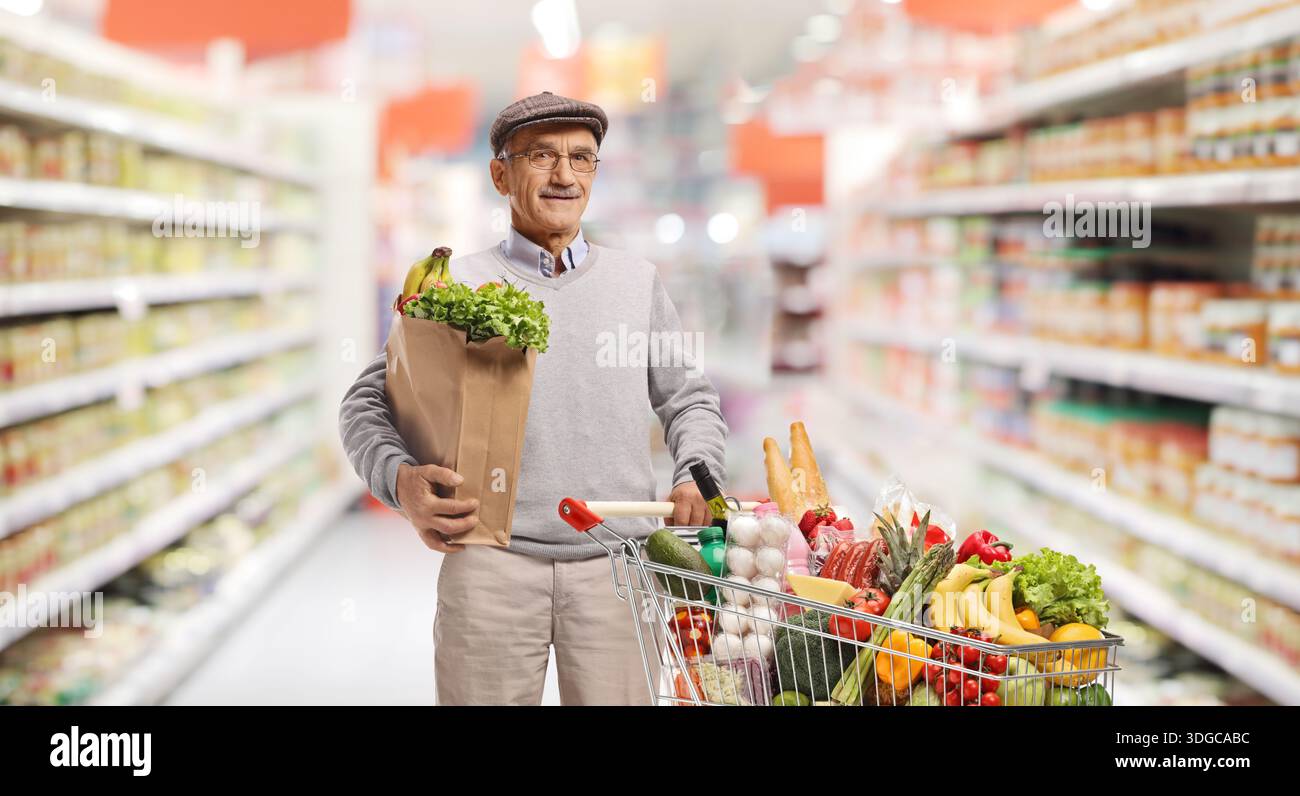 Uomo anziano che fa acquisti di generi alimentari in un supermercato con carrello e sacchetto di carta Foto Stock