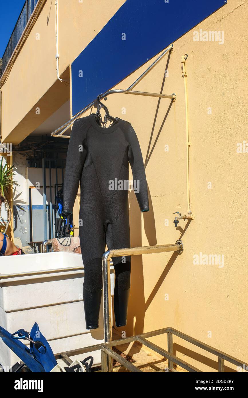Sullo sfondo di una parete gialla e di varie attrezzature per le immersioni, una muta si asciuga dopo essersi immersa in mare. Foto Stock