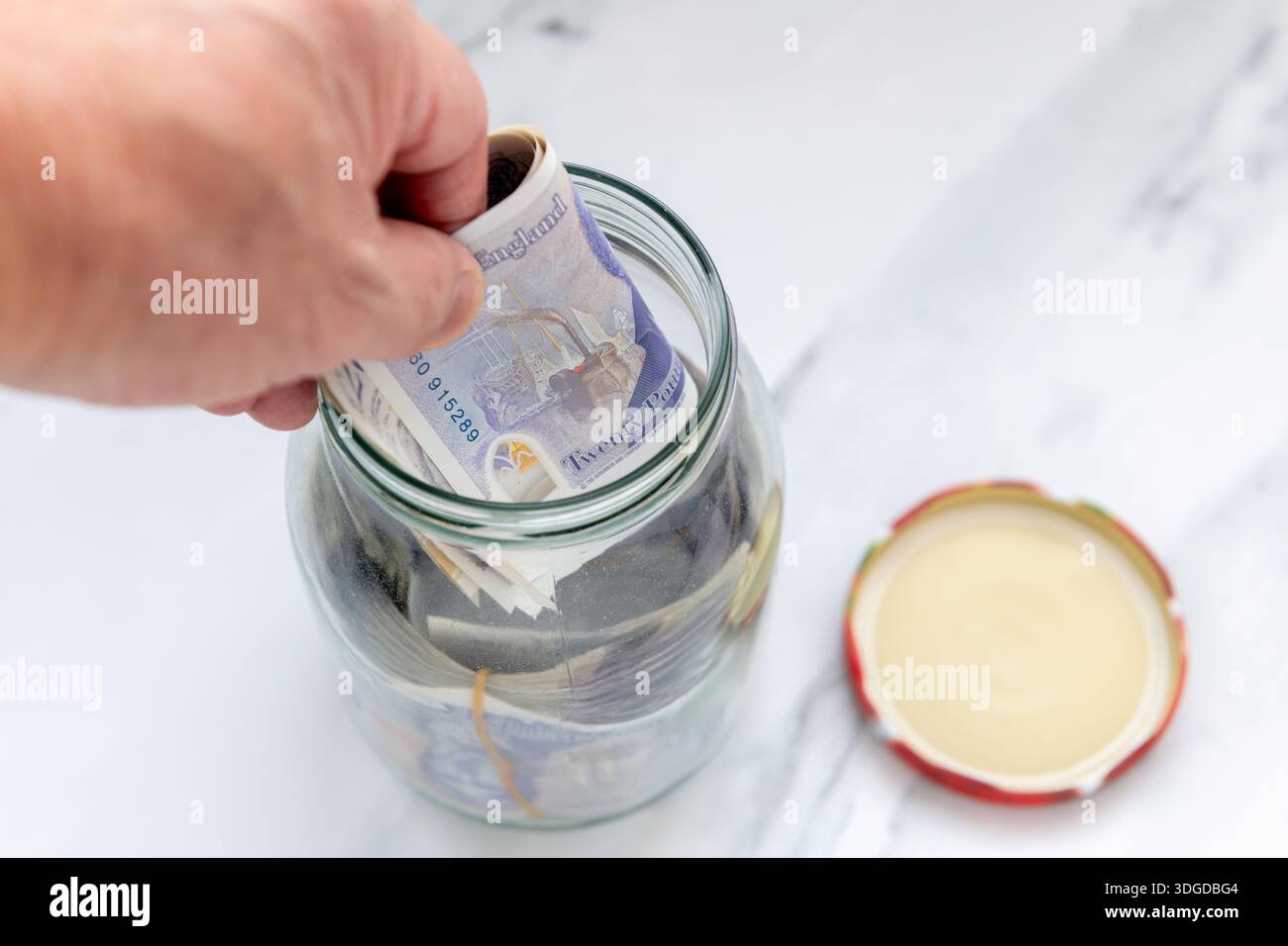 Una persona che mette banconote in un vaso di vetro. Foto Stock