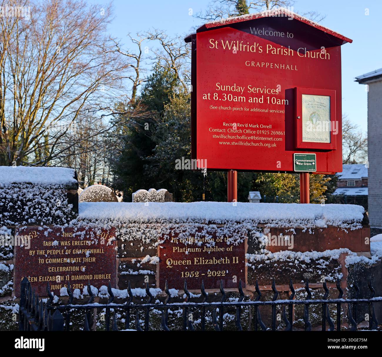 Insegna per la chiesa parrocchiale di St Wilfrid nel villaggio di Grappenhall vicino a Warrington, Cheshire, fotografata in inverno con la neve a terra, con monumenti commemorativi Foto Stock