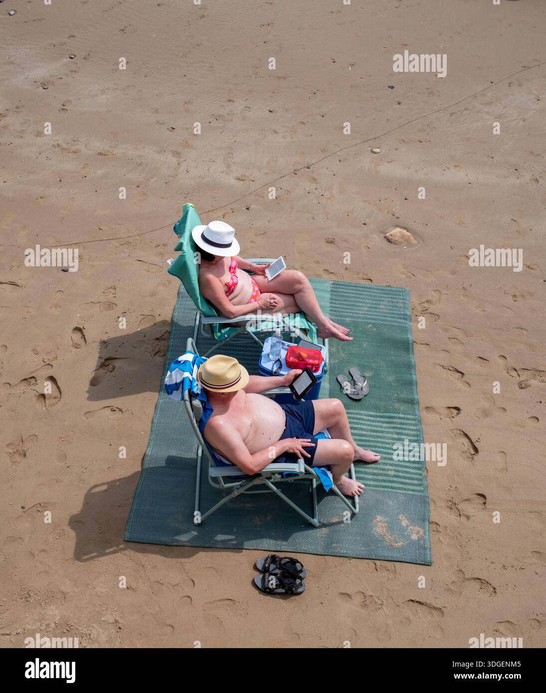 Coppia che legge eBook su Kindle ebook readers sulla spiaggia di Saundersfoot Pembrokeshire West Wales UK Foto Stock