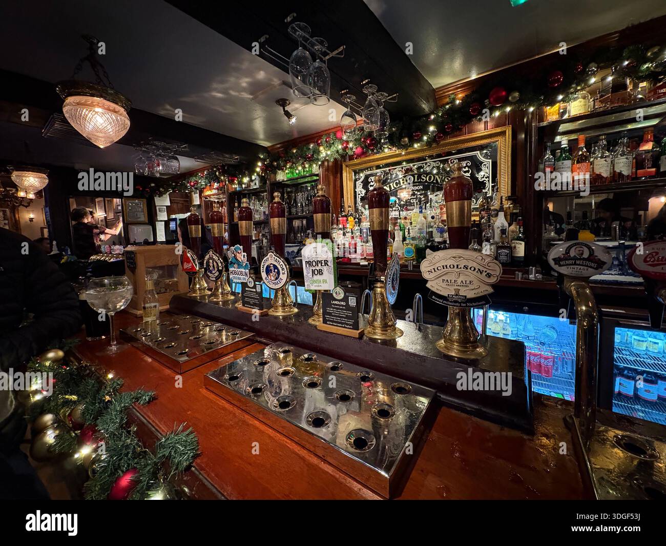 Tradizionale pub britannico interno con bancone bar decorato, birrerie e bottiglie, che creano un'atmosfera calda e accogliente durante la serata Foto Stock