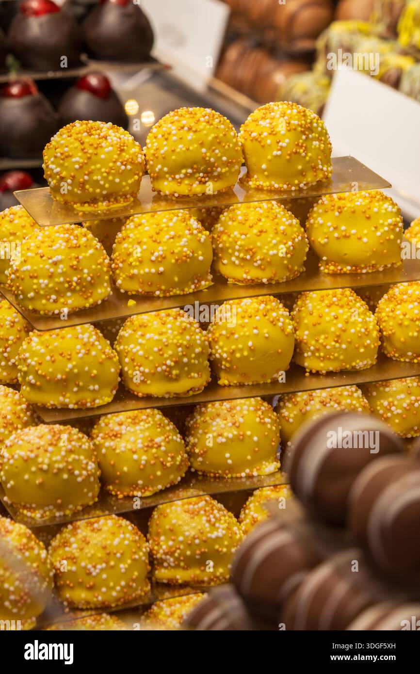 Tartufi di cioccolato giallo con spolverini di zucchero disposti sugli scaffali esposti in una vetrina di pasticceria Foto Stock
