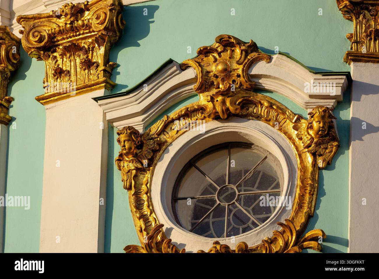 Ornamento barocco dorato sulla facciata della chiesa di Sant'Andrea a Kiev, Ucraina. Due cherubini incorniciano una finestra circolare, con un'ornata capitale corinzia Foto Stock