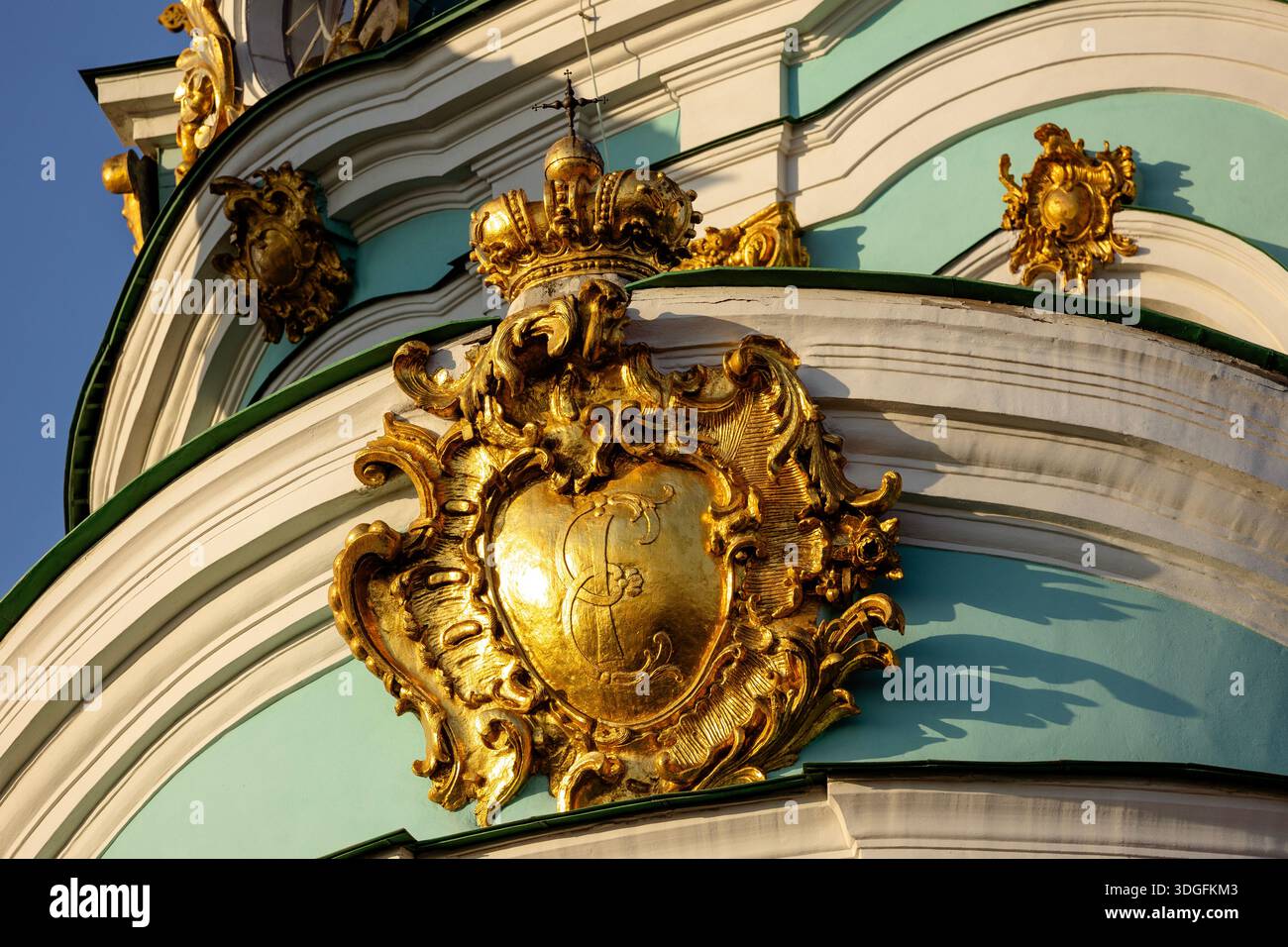 Primo piano di un cartiglio barocco dorato sulla facciata della chiesa di Sant'Andrea a Kiev, Ucraina. Il dettaglio ornato presenta il monogramma reale dell'imperatrice Foto Stock
