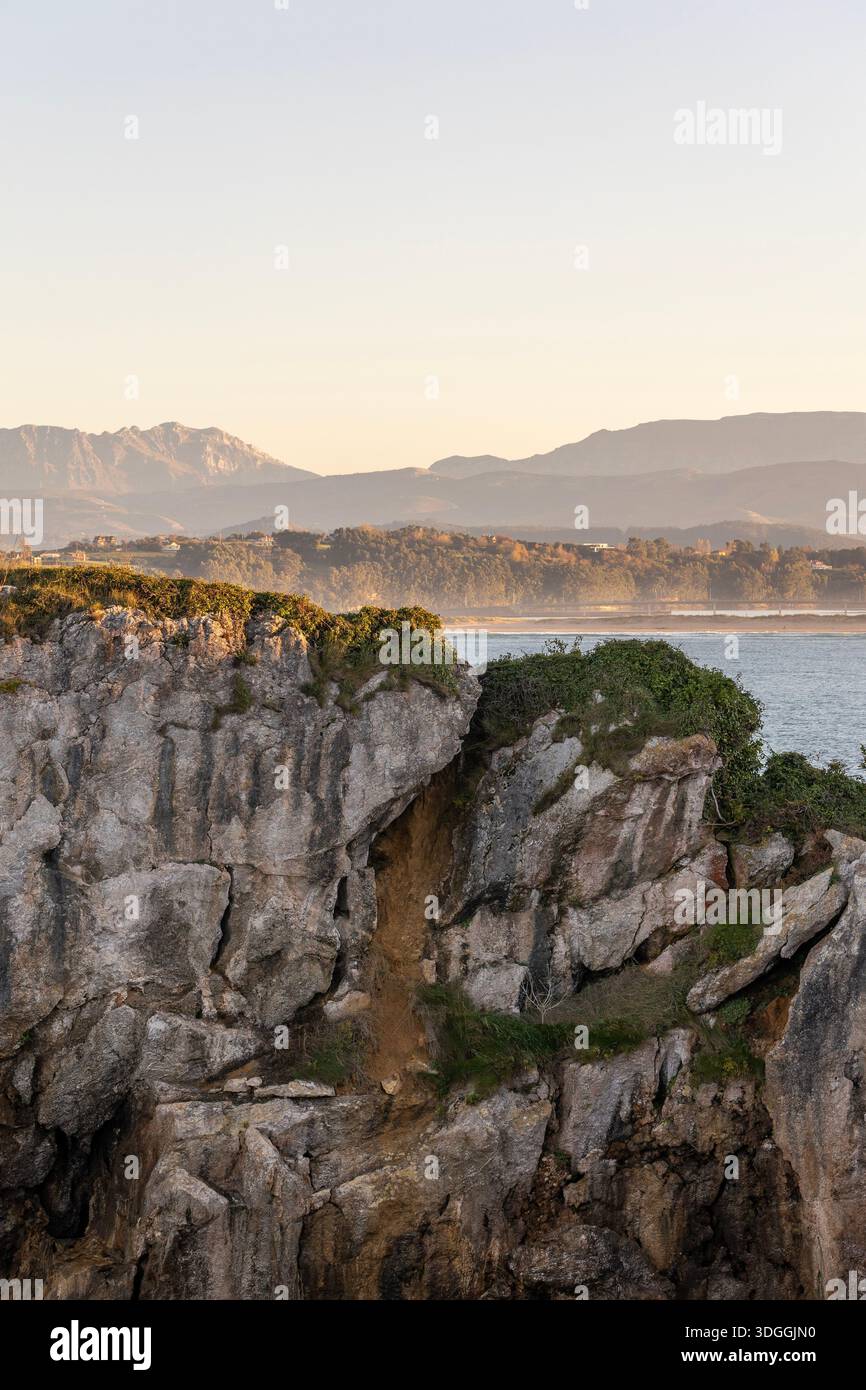 Una vista panoramica delle scogliere rocciose sulla penisola di Magdalena a Santander, in Spagna, con la baia e le montagne nebbiose sullo sfondo al tramonto. Foto Stock