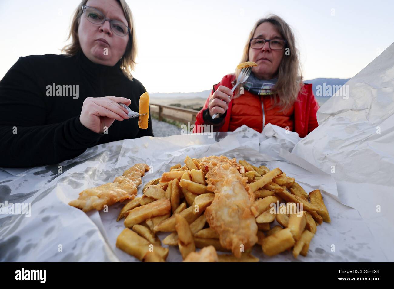 Due donne che si godono il fish 'n' chips sulla spiaggia di Kaikoura, Kaikoura, Canterbury, nuova Zelanda Foto Stock