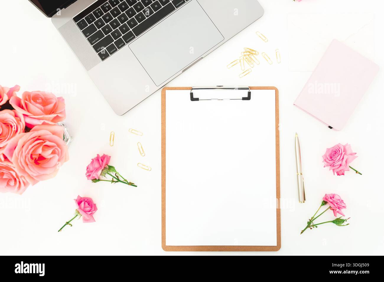 Spazio di lavoro elegante e femminile con laptop, appunti e rose su una scrivania bianca e un arredo creativo per l'ufficio domestico Foto Stock