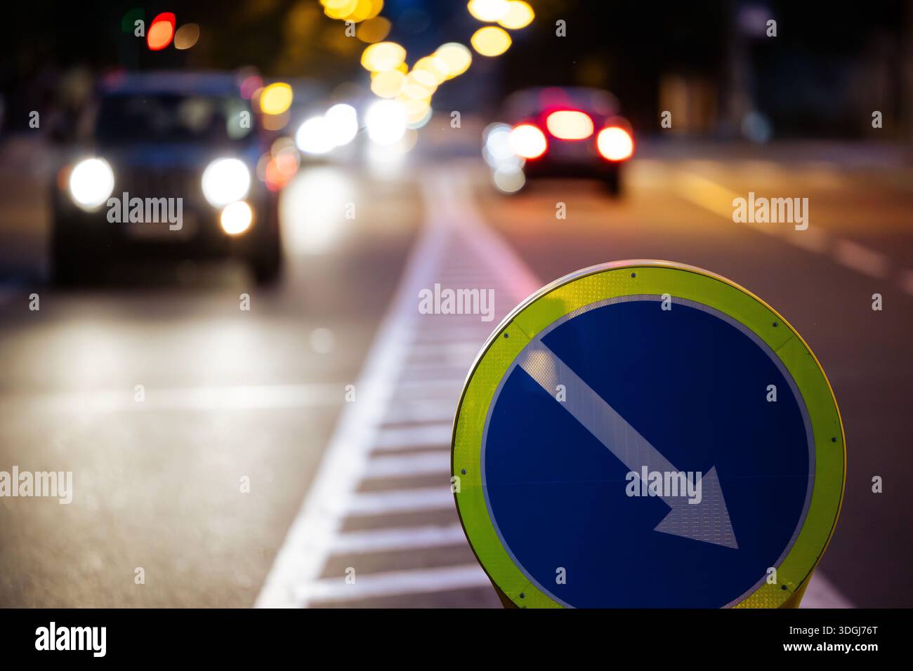 Primo piano di una freccia blu temporanea su una strada di notte. Questo cartello rifrangente guida il traffico notturno, con fari per auto e tai Foto Stock