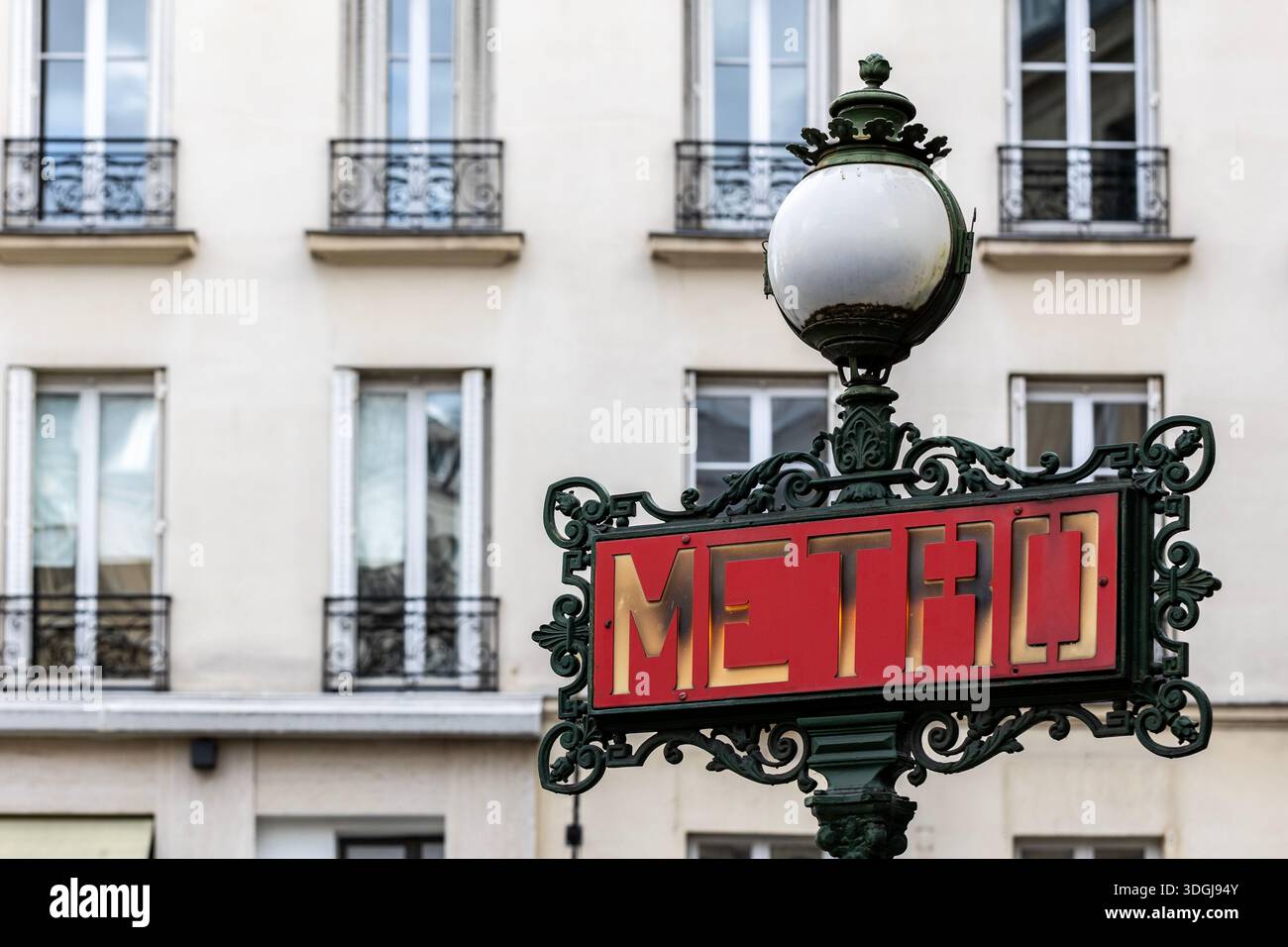Un bellissimo cartello della metropolitana Art Nouveau con ornati lavori in ferro, adagiato sull'elegante facciata di un classico edificio di appartamenti parigino. Un concetto di tempo Foto Stock