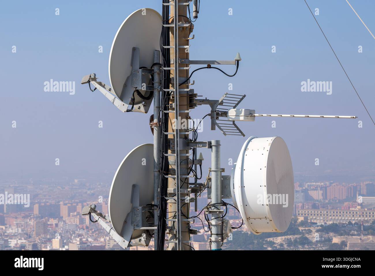 Una torre di telecomunicazioni con varie antenne relè a microonde, tra cui diverse parabole paraboliche e una grande antenna racchiusa in un radome, che si affaccia su un'estensione Foto Stock