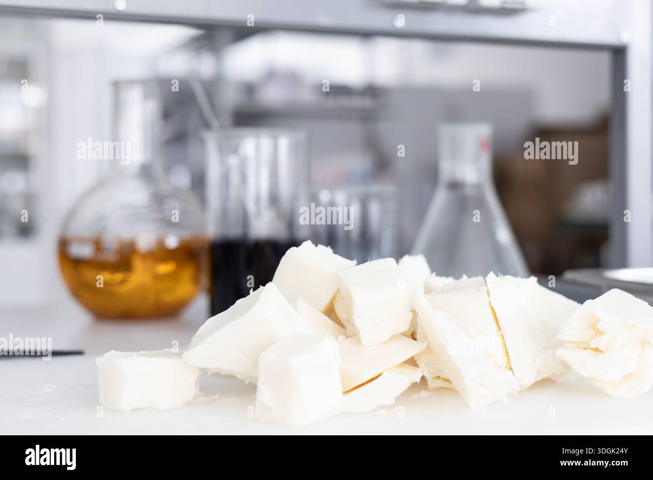 Il burro di karitè crudo, tagliato a pezzi, si trova su un tagliere bianco in un laboratorio. Questo ingrediente è per la produzione artigianale di cosmetici biologici, con spirito Foto Stock