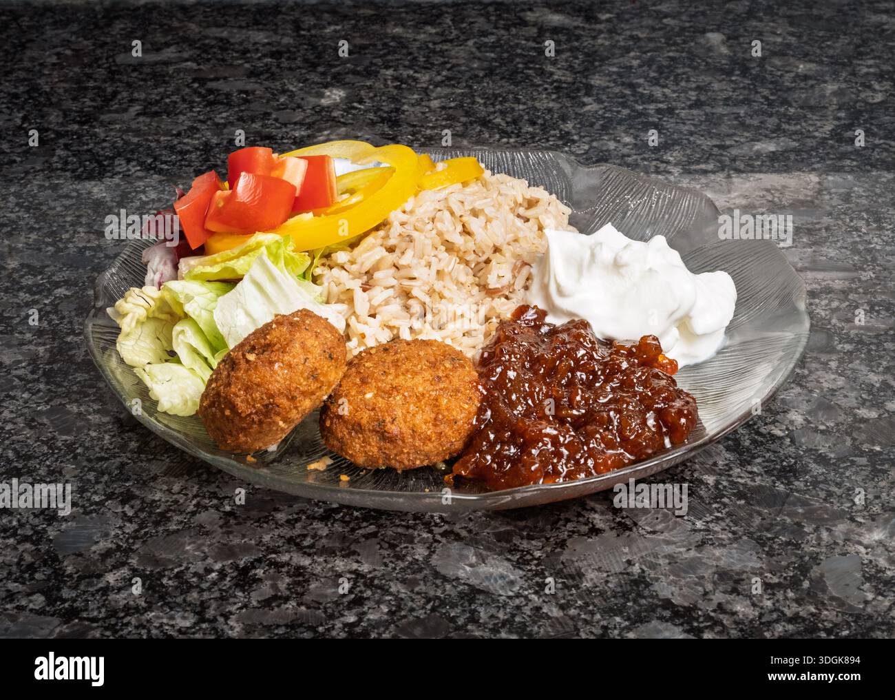 Fotografia commerciale di un piatto di falafel servito con chutney dolce, panna acida e verdure fresche su granito. Foto Stock
