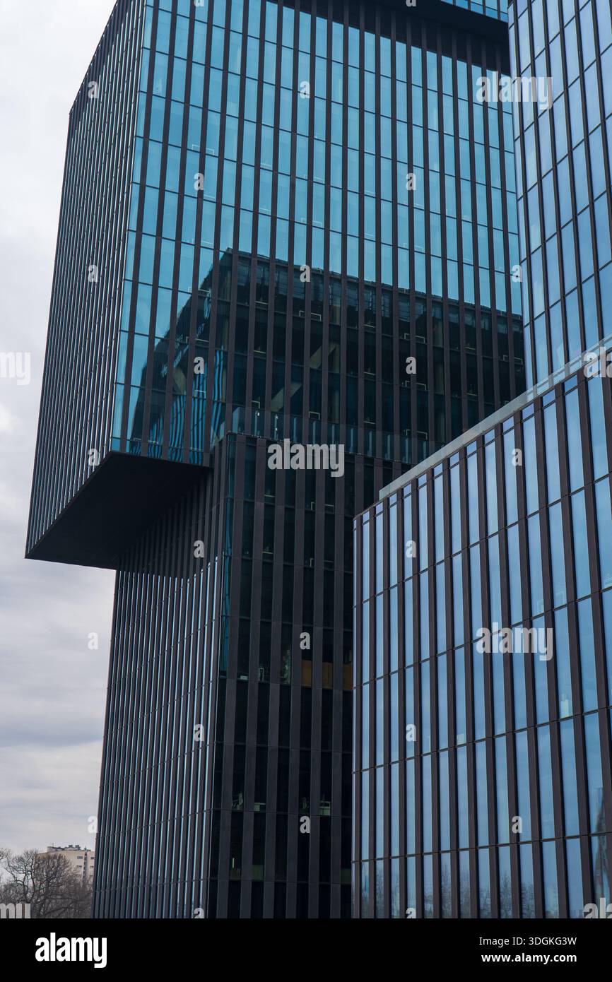 La torre in vetro e acciaio di Katowice, Polonia, mostra pinne verticali e una sezione superiore a sbalzo. I finestrini riflettenti riflettono le facciate sotto il telaio coperto Foto Stock