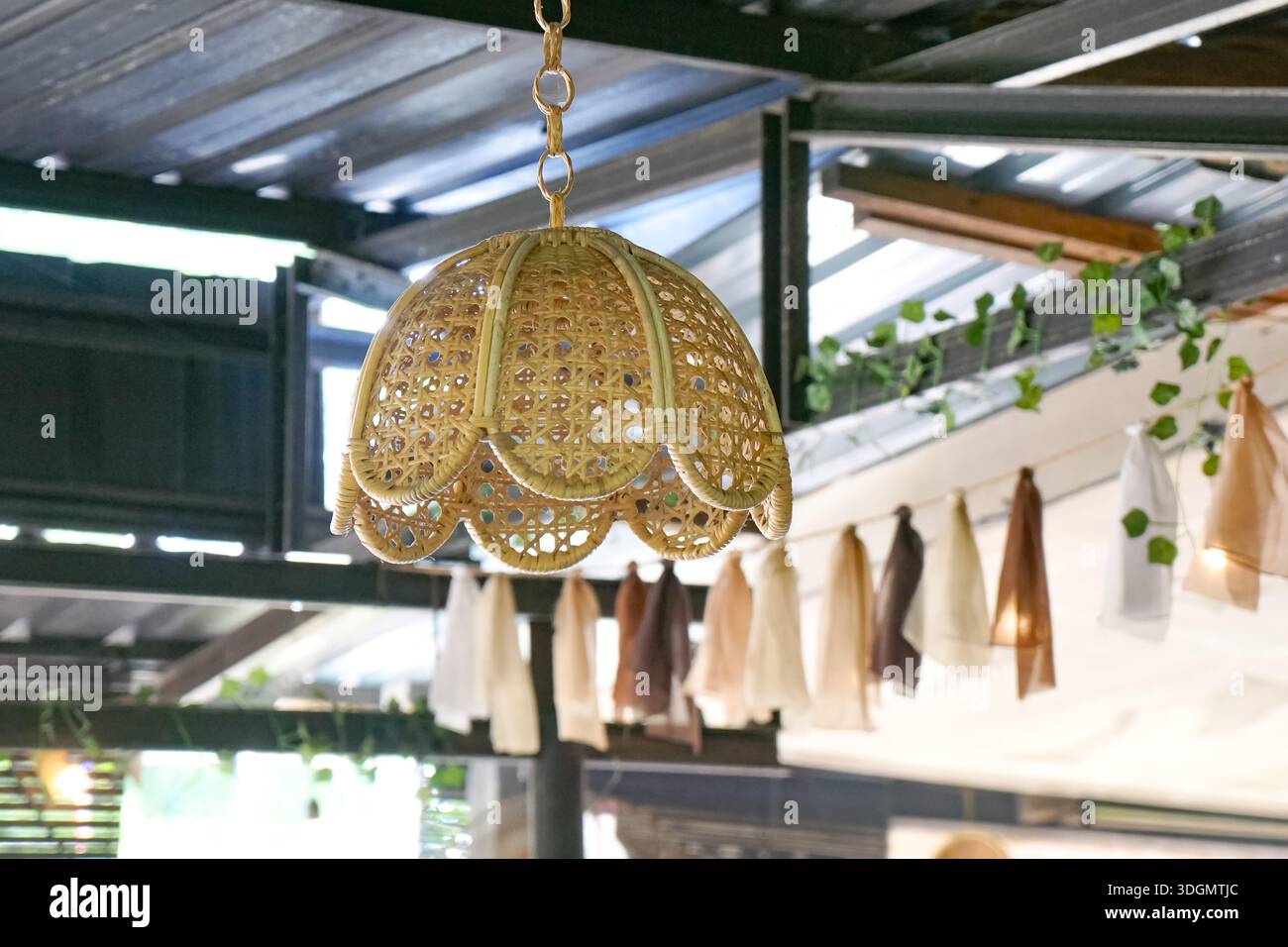 Lampada in rattan intrecciato con bordi smerlati appesi in uno spazio esterno accogliente e decorato con viti. Foto Stock