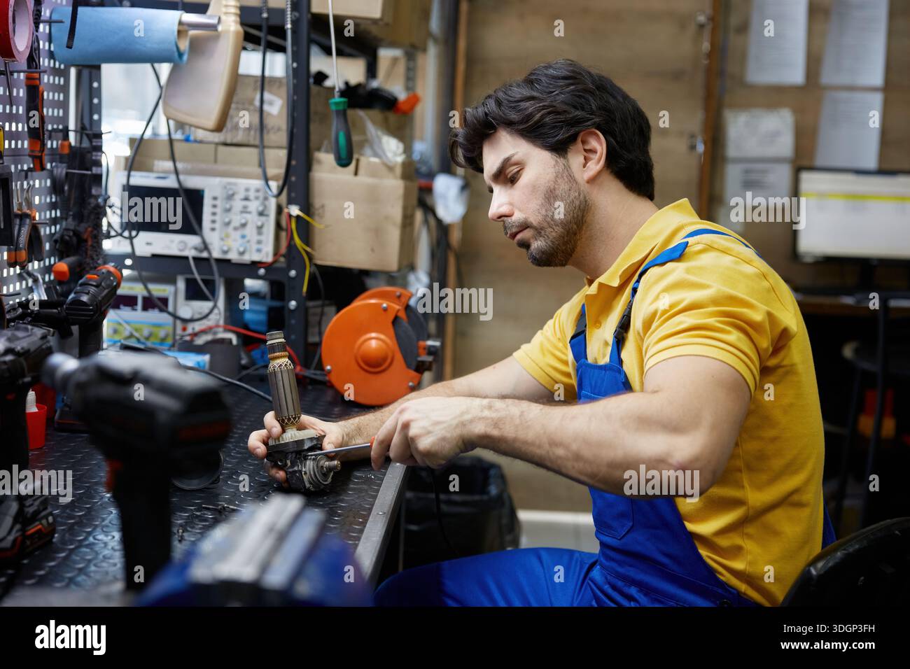 Tecnico addetto all'assistenza che ripara un trapano elettrico rotto all'interno di un'officina occupata Foto Stock
