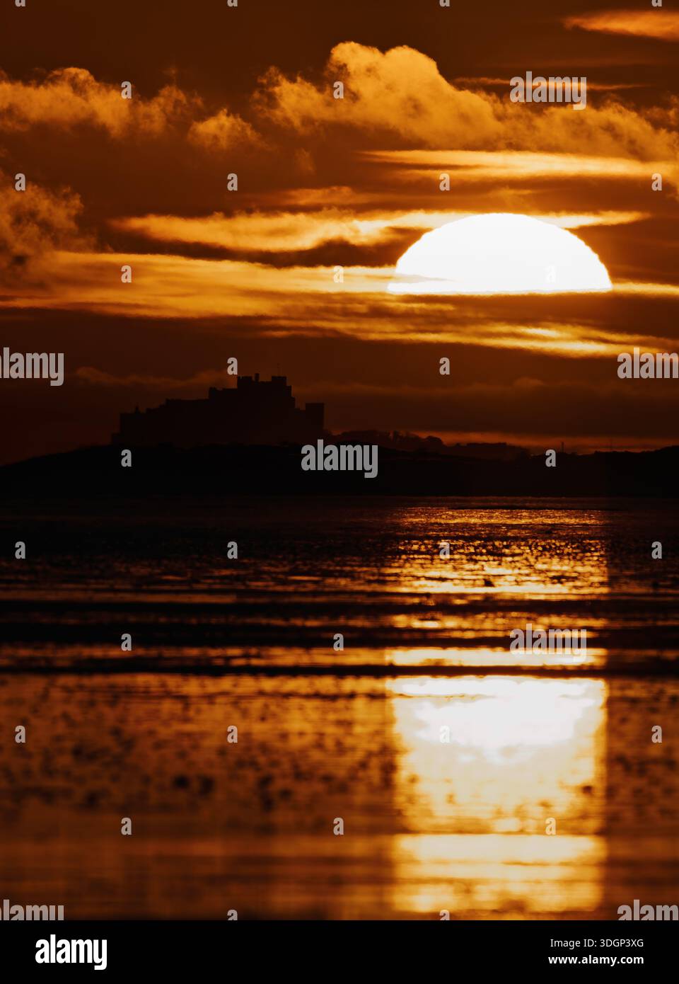 Il castello di Bamburgh si staglia contro il sole nascente, Northumberland Foto Stock