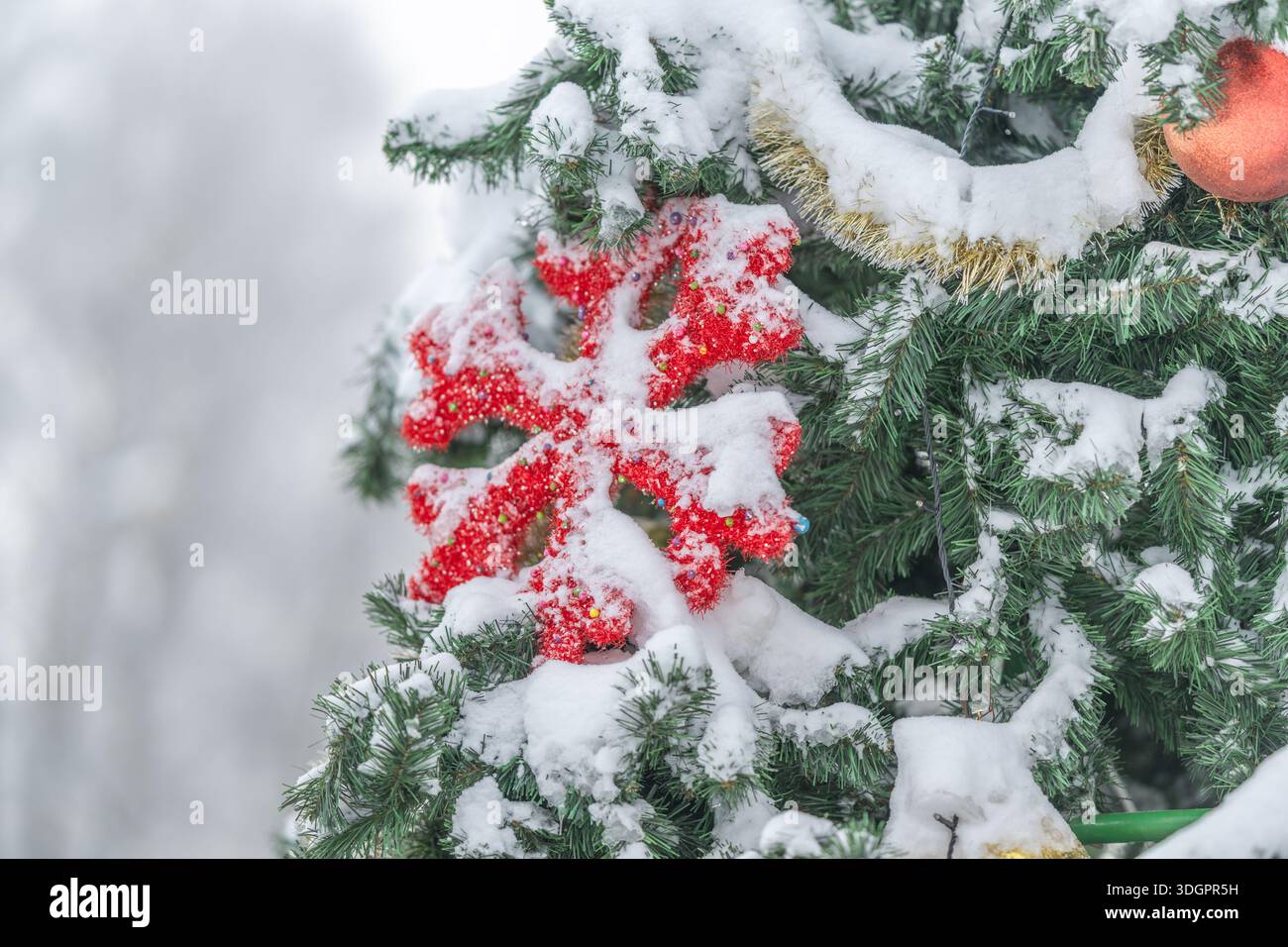 Ornamento rosso fiocco di neve spolverato di neve, fantasie intricate che contrastano il verde, vivaci dettagli stagionali, tonalità fredde e vivaci, fascino divertente per le vacanze Foto Stock