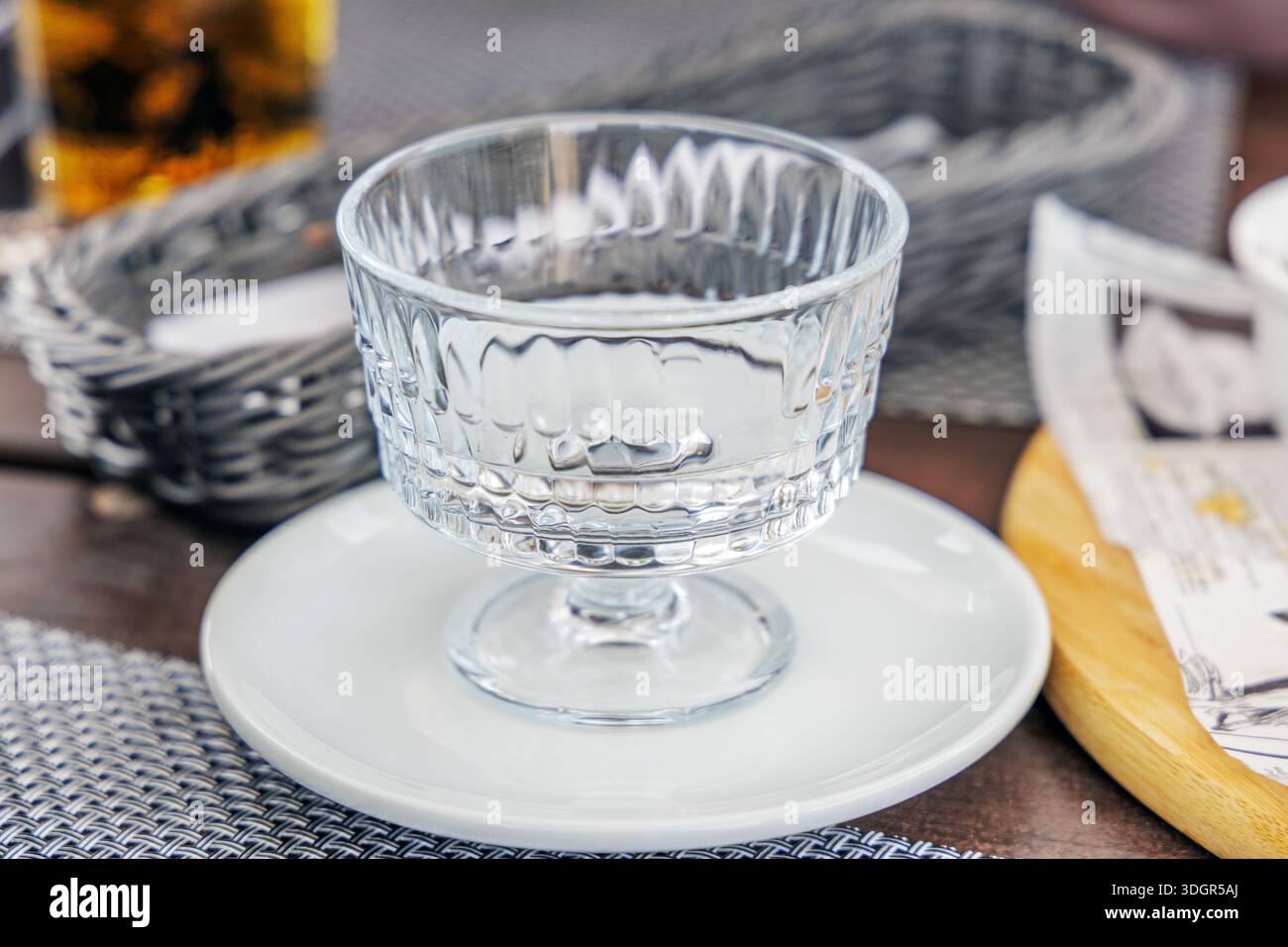 Elegante ciotola di vetro vuota in stile vintage su un piatto bianco in un ambiente da caffè. Perfetto per il servizio di ristorazione, il catering e i concetti di marketing dell'ospitalità. Foto Stock