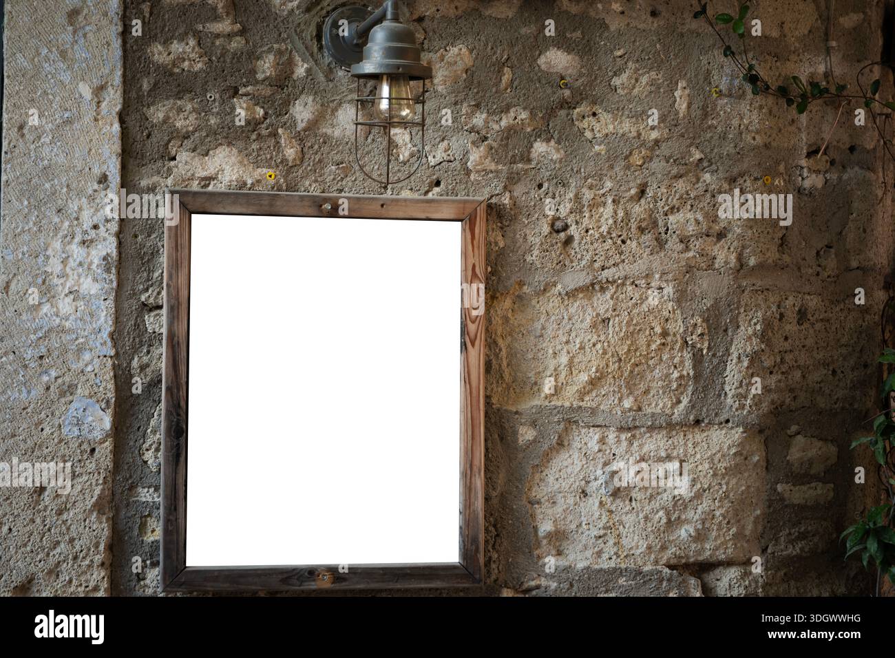 Telaio in legno vuoto con spazio per le copie appeso su una parete rustica in pietra testurizzata, illuminato da una lampada da parete d'epoca per un mockup display Foto Stock