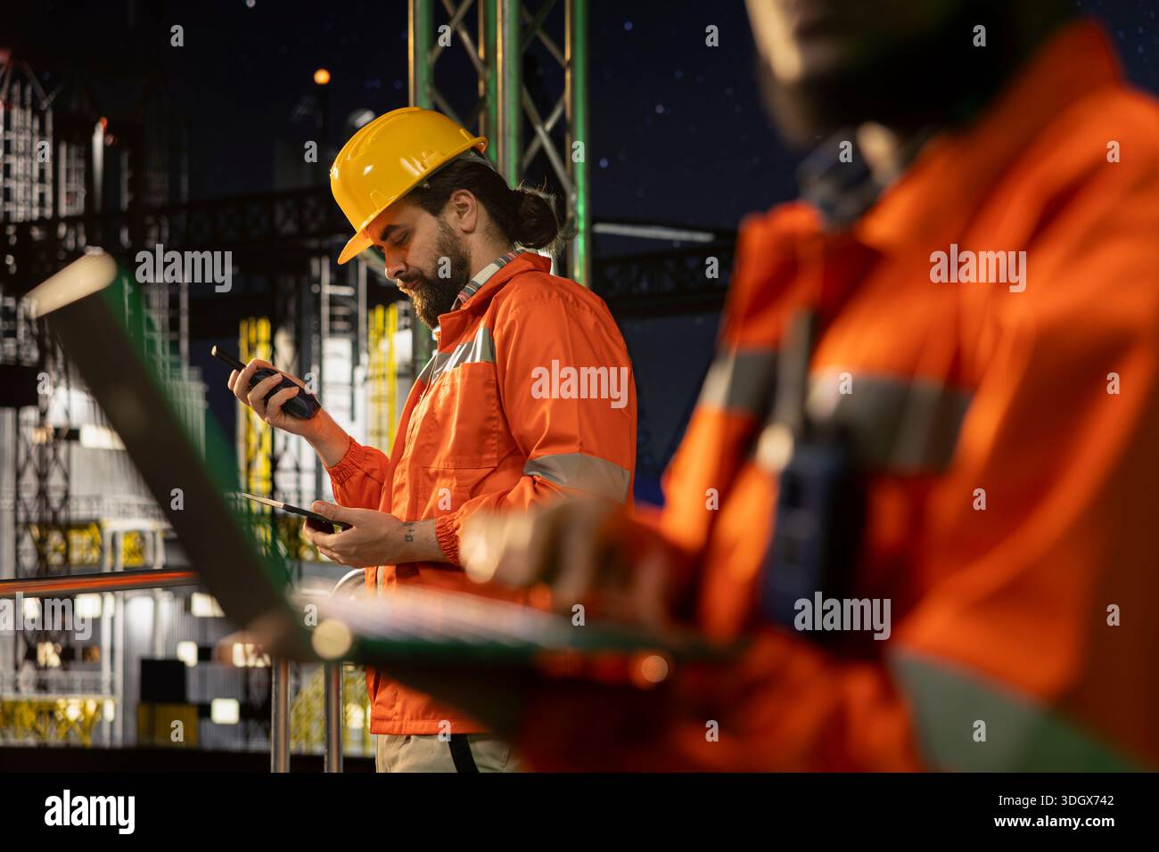 Primo piano di uno specialista di navi di perforazione industriale che ispeziona l'integrità dell'infrastruttura utilizzando un computer portatile. Colleghi della piattaforma offshore che eseguono controlli dei macchinari per garantire la sicurezza durante le operazioni notturne Foto Stock