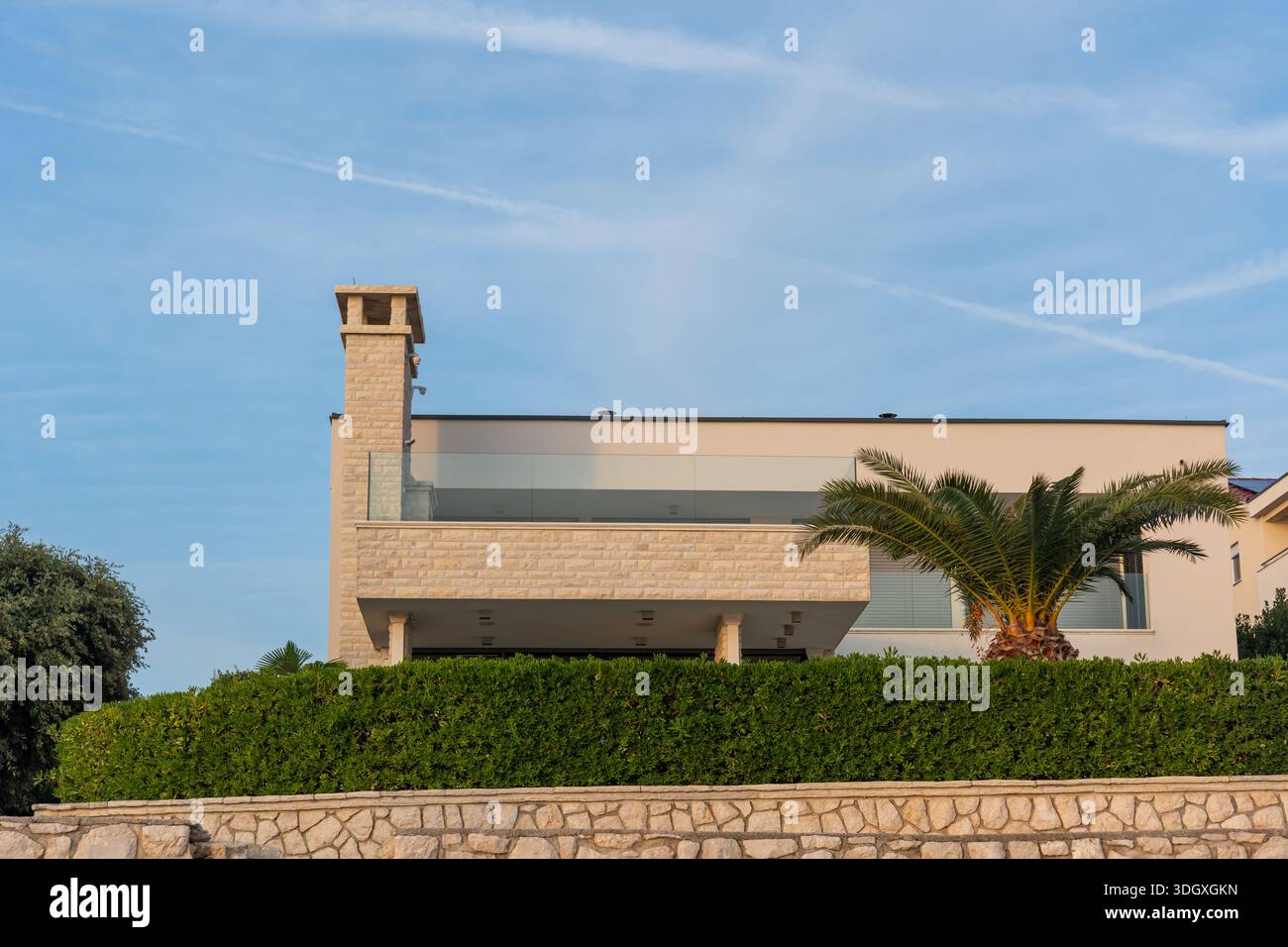Moderna casa sul mare con recinzione in pietra e palma sotto il cielo azzurro. Immobili costieri, casa per le vacanze, proprietà di lusso e lifest mediterraneo Foto Stock