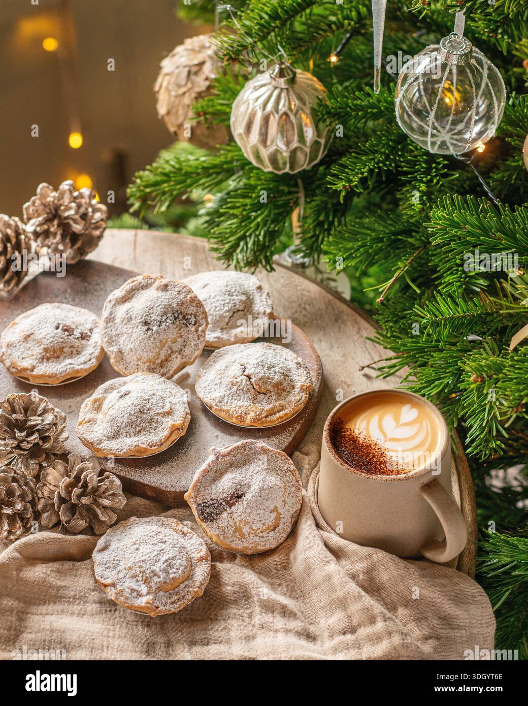 Una selezione di torte natalizie spolverate con zucchero a velo, disposte su una tavola di legno con rami di pino, pinne e calde luci natalizie. Foto Stock