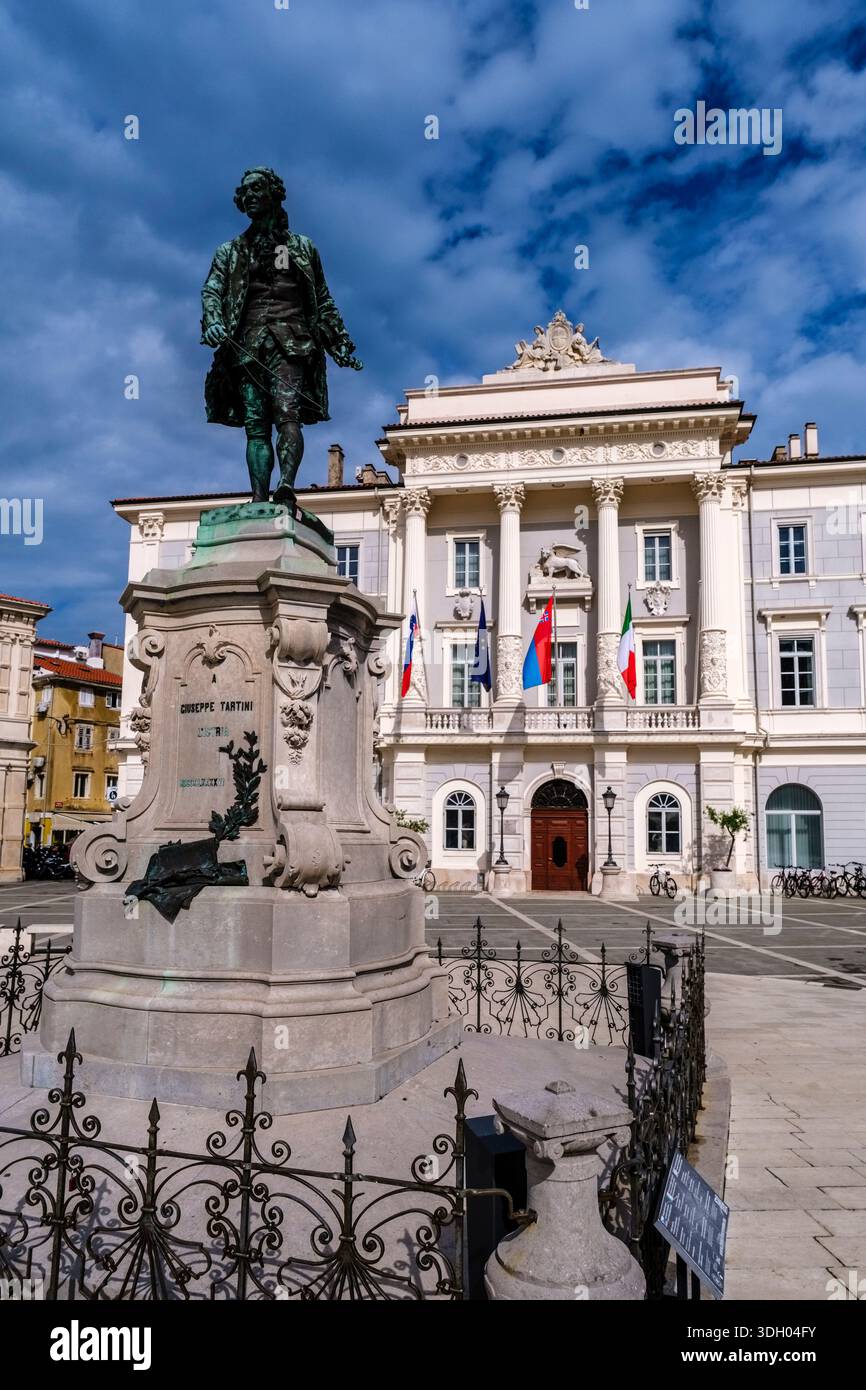 Monumento in bronzo di Giuseppe Tartini di fronte al Municipio sulla piazza centrale dei Tartini con facciata neoclassica e varie bandiere che sventolano in dista Foto Stock