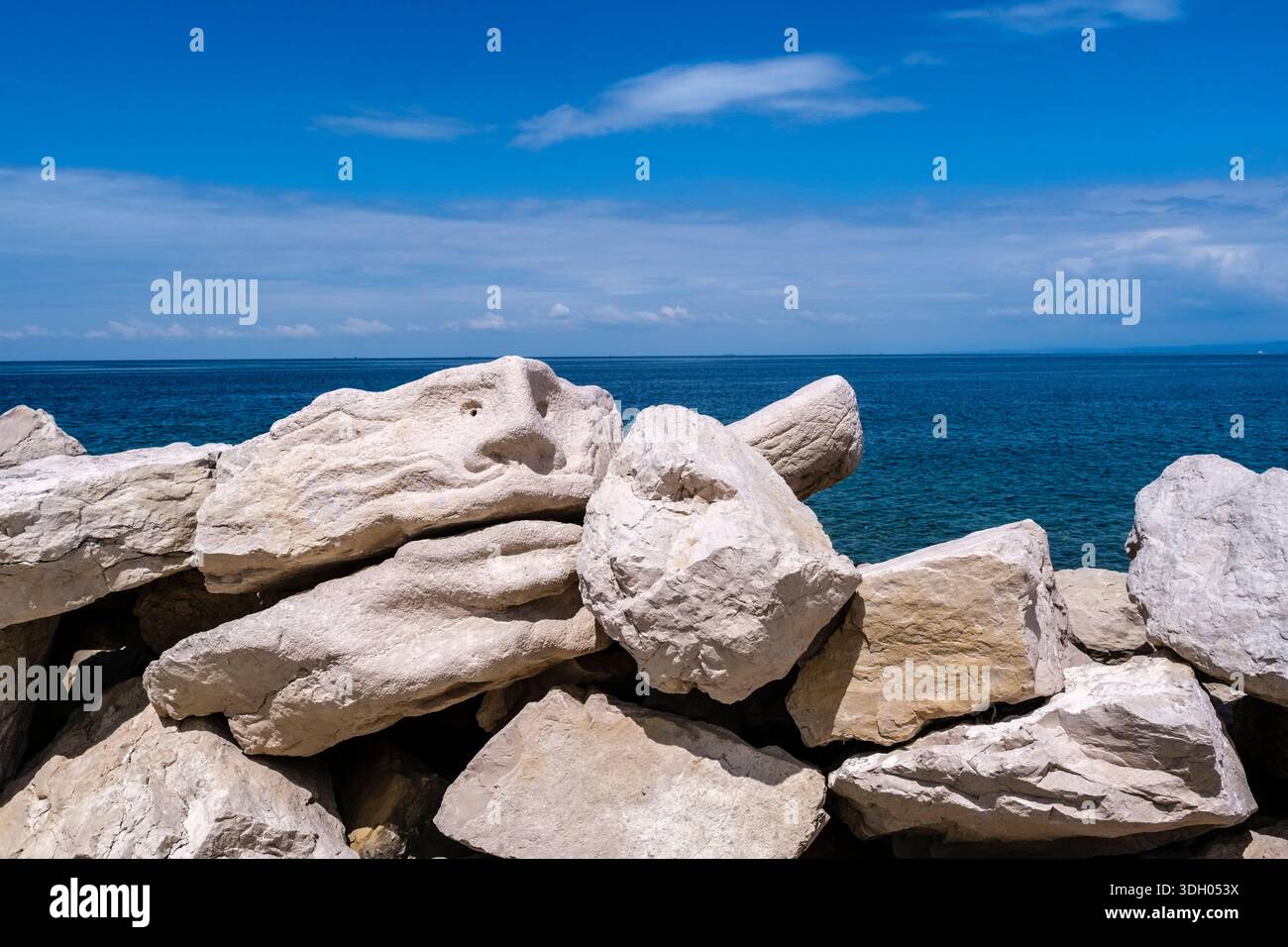 Primo piano di grandi rocce calcaree bianche con sculture scolpite nella roccia lungo la costa con il mare blu e l'orizzonte in lontananza. Foto Stock