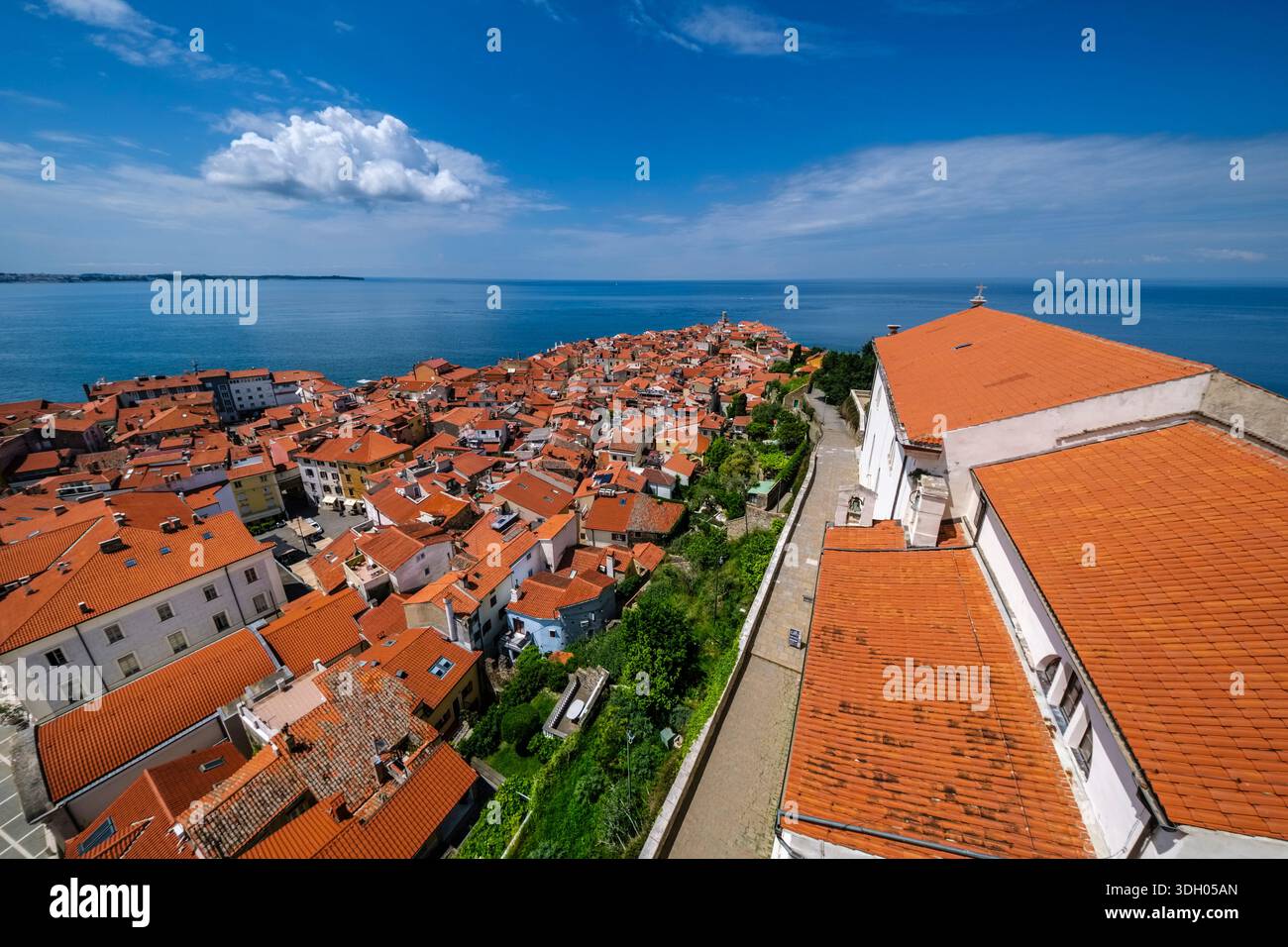 Vista dall'alto dei tetti con tegole rosse, il lato della chiesa parrocchiale di San Giorgio e la costa che si estende in lontananza. Foto Stock