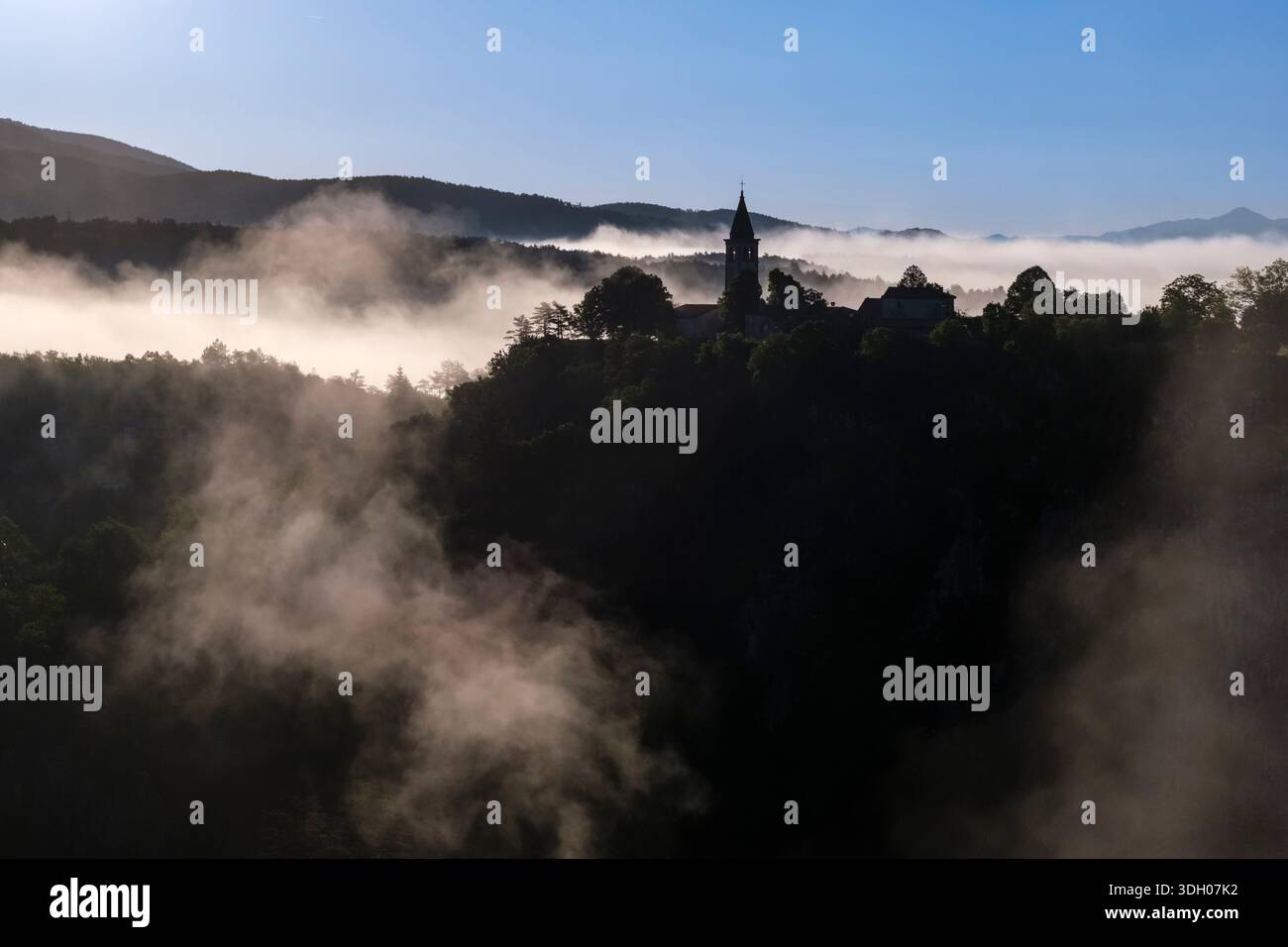 Sagoma della chiesa di San Canziano e del villaggio di Skocjan che si innalza sopra la fitta nebbia mattutina in lontananza. Foto Stock