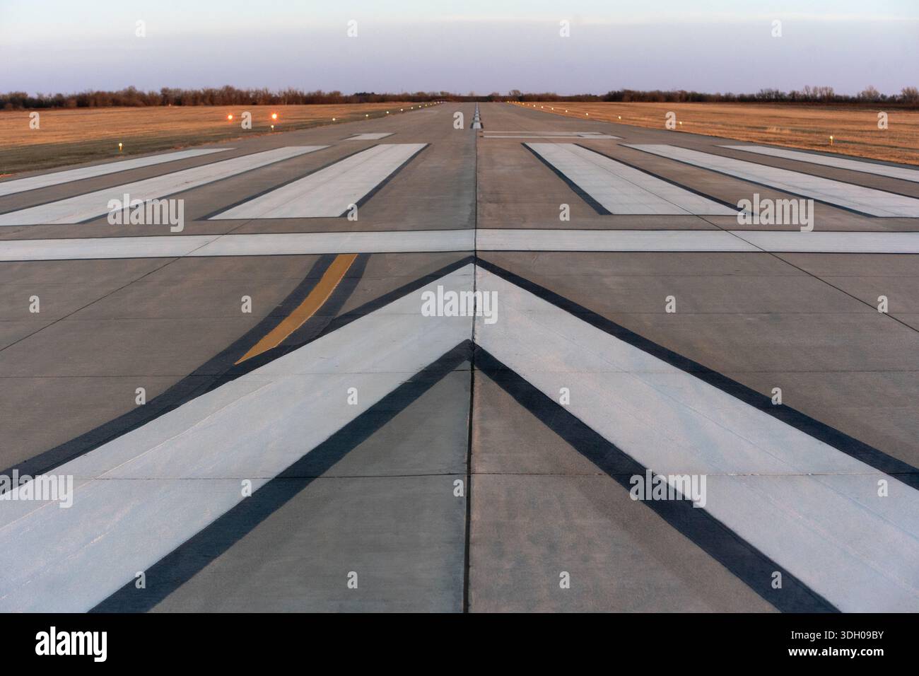 Pista con frecce direzionali bianche al crepuscolo sul campo d'aviazione vuoto Foto Stock