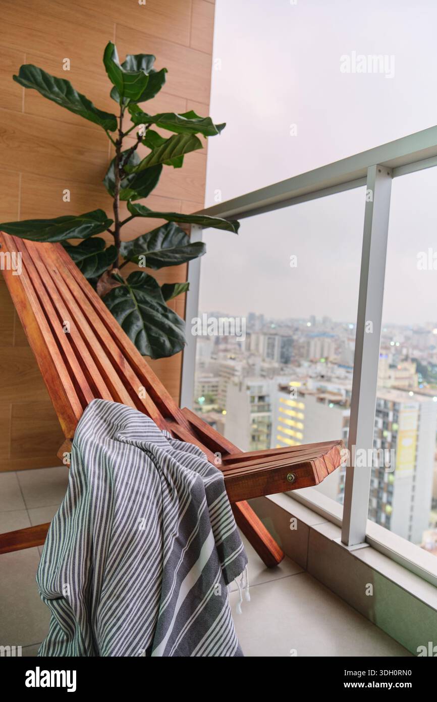 Balcone con sedia in legno e pianta di ficus lyrata che si affaccia sullo skyline della città Foto Stock
